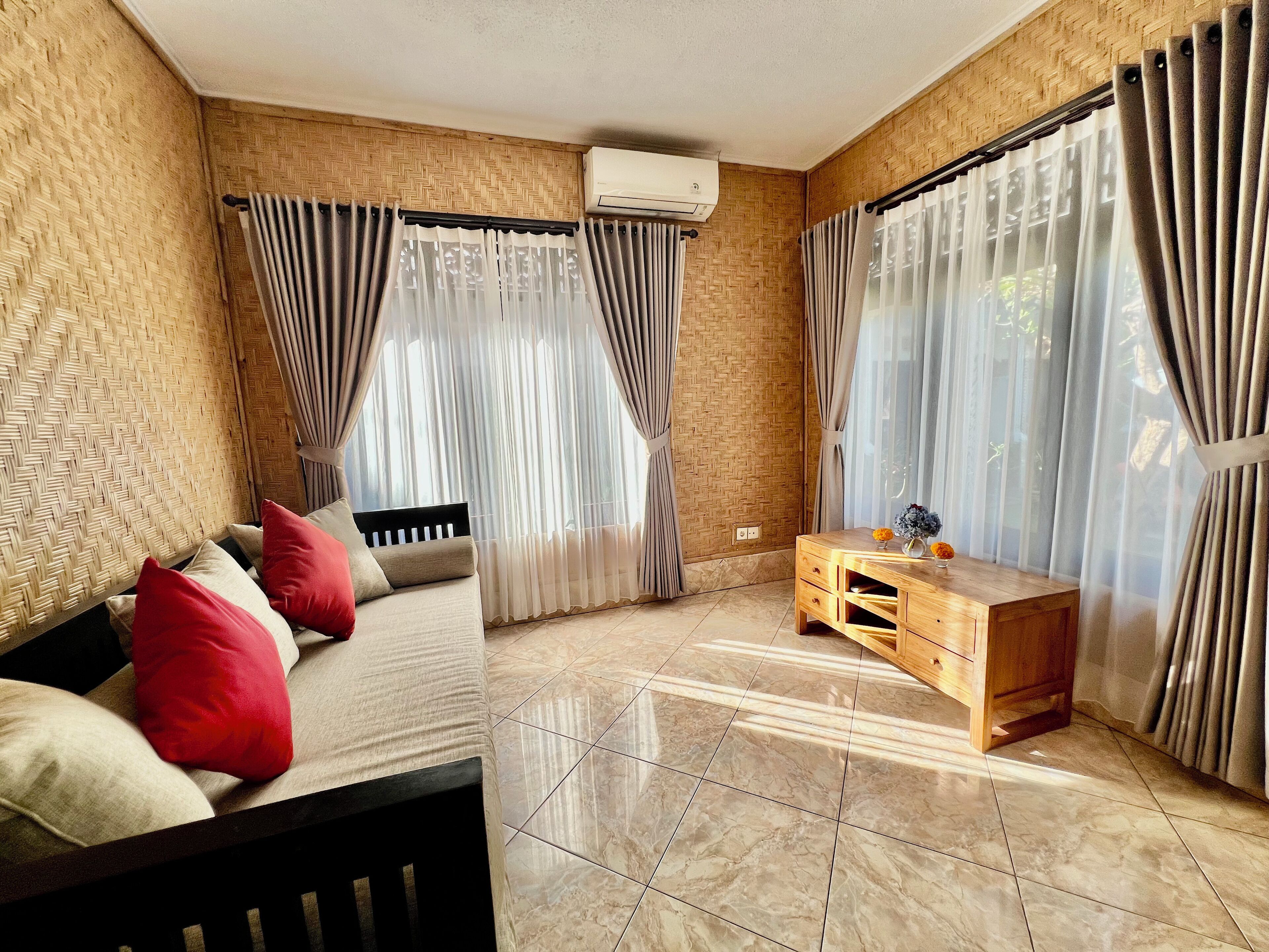 A room with a sofa, a wooden cabinet, and a window with sheer curtains.