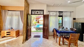 A dining area with a table set for two, a wooden cabinet, and a view of a swimming pool. - Villa Tiga Naga Sanur (Denpasar)