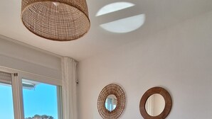 Uma sala de estar moderna com um sofá cinza, uma mesa de centro de vidro e dois espelhos fixados na parede.