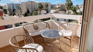 Varanda com móveis de vime e mesa de vidro, com vista para uma área residencial com edifícios e palmeiras.
