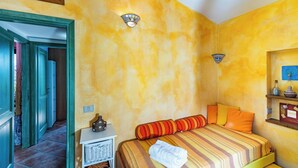 Una habitación con una cama, una mesita de noche, una lámpara de pared y un estante con objetos decorativos.