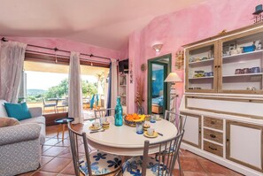 A room with a dining table set for four, a sofa, a cabinet with dishes, and a view of the outdoors. - Belvedere With A Stunning View (Loiri Porto San Paolo)