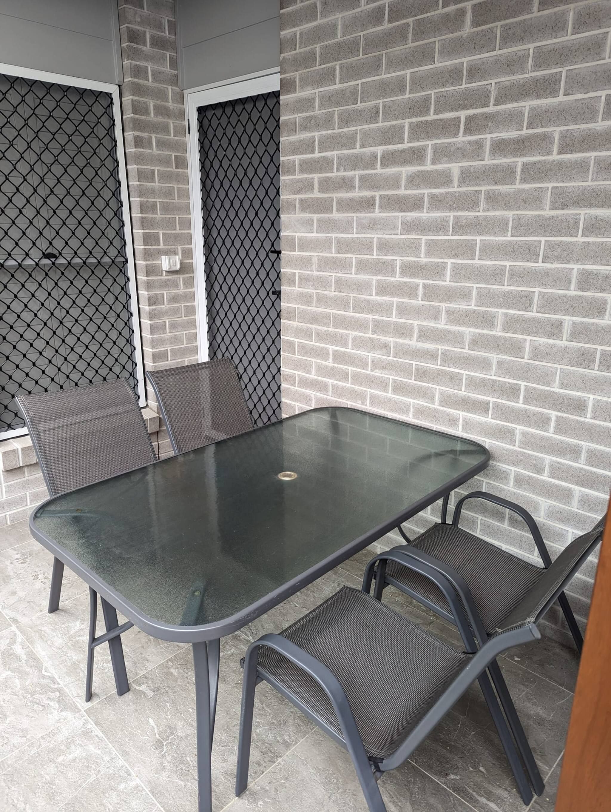 A patio area with a glass-top table and four chairs, a brick wall, and a metal gate.