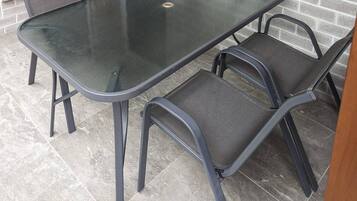 A patio area with a glass-top table and four chairs, a brick wall, and a metal gate.