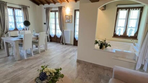 A spacious room with a wooden ceiling, a dining area with a table and chairs, a small sitting area with a bench, and a window with curtains. - Casale Antica Cassia Beauty Spa (Roma)