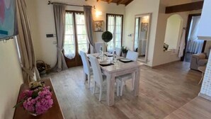 A dining area with a wooden table and chairs, a vase of flowers, and a view of the adjacent room. - Casale Antica Cassia Beauty Spa (Roma)