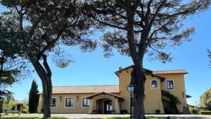 A yellow building with a tiled roof, surrounded by trees and a clear blue sky. - Casale Antica Cassia Beauty Spa (Roma)