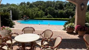A patio area with a round table and chairs, a brick wall, and a pool in the background. - Casale Antica Cassia Beauty Spa (Roma)