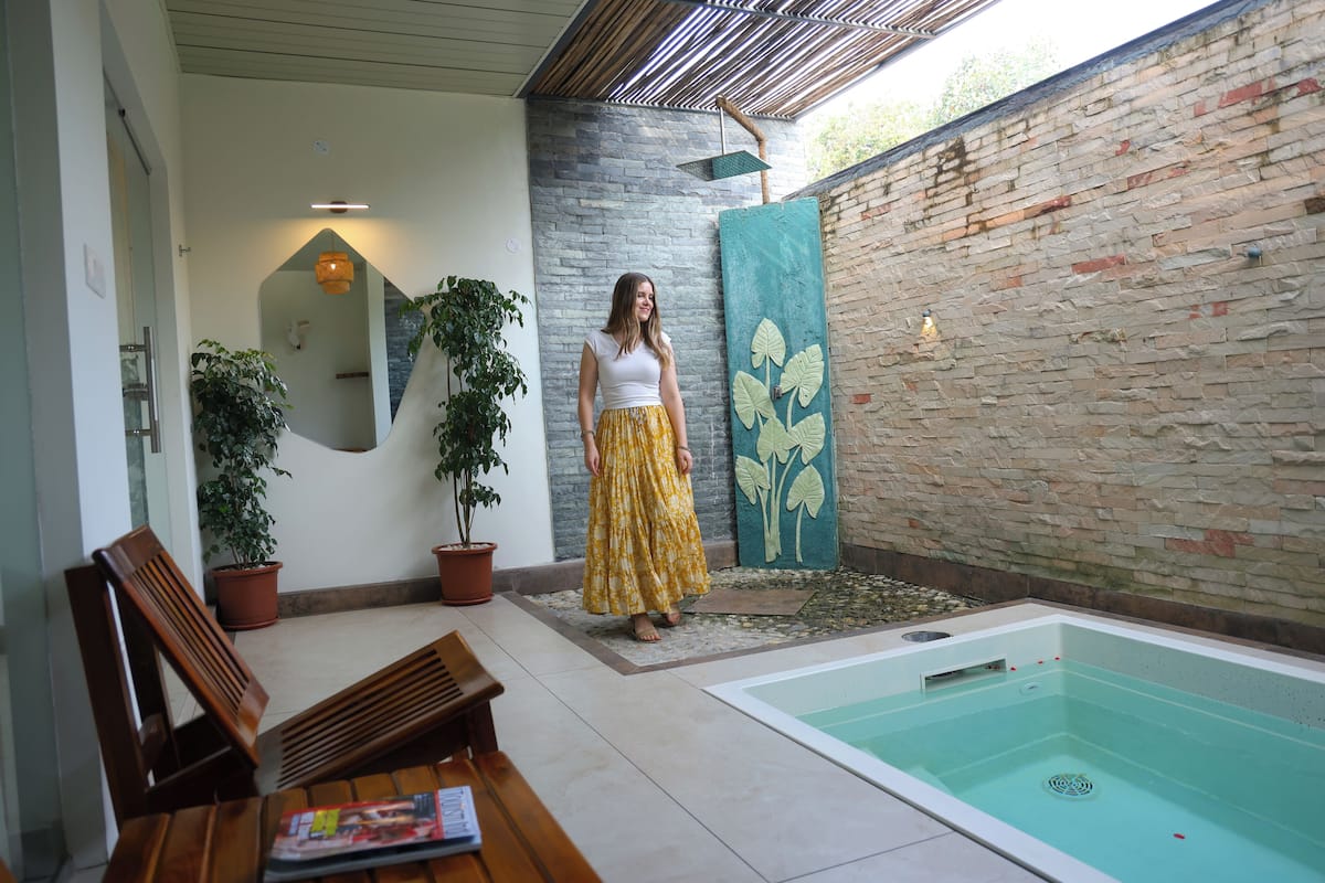 Une personne se tient près d’un espace de détente avec une piscine, un banc en bois et des plantes en pot.