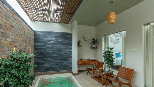 Een modern interieur met een stenen muur, een zwart gestructureerd muur, een houten tafel met stoelen, een tafel met glazen blad en een klein binnenzwembad met rode drijvende objecten.