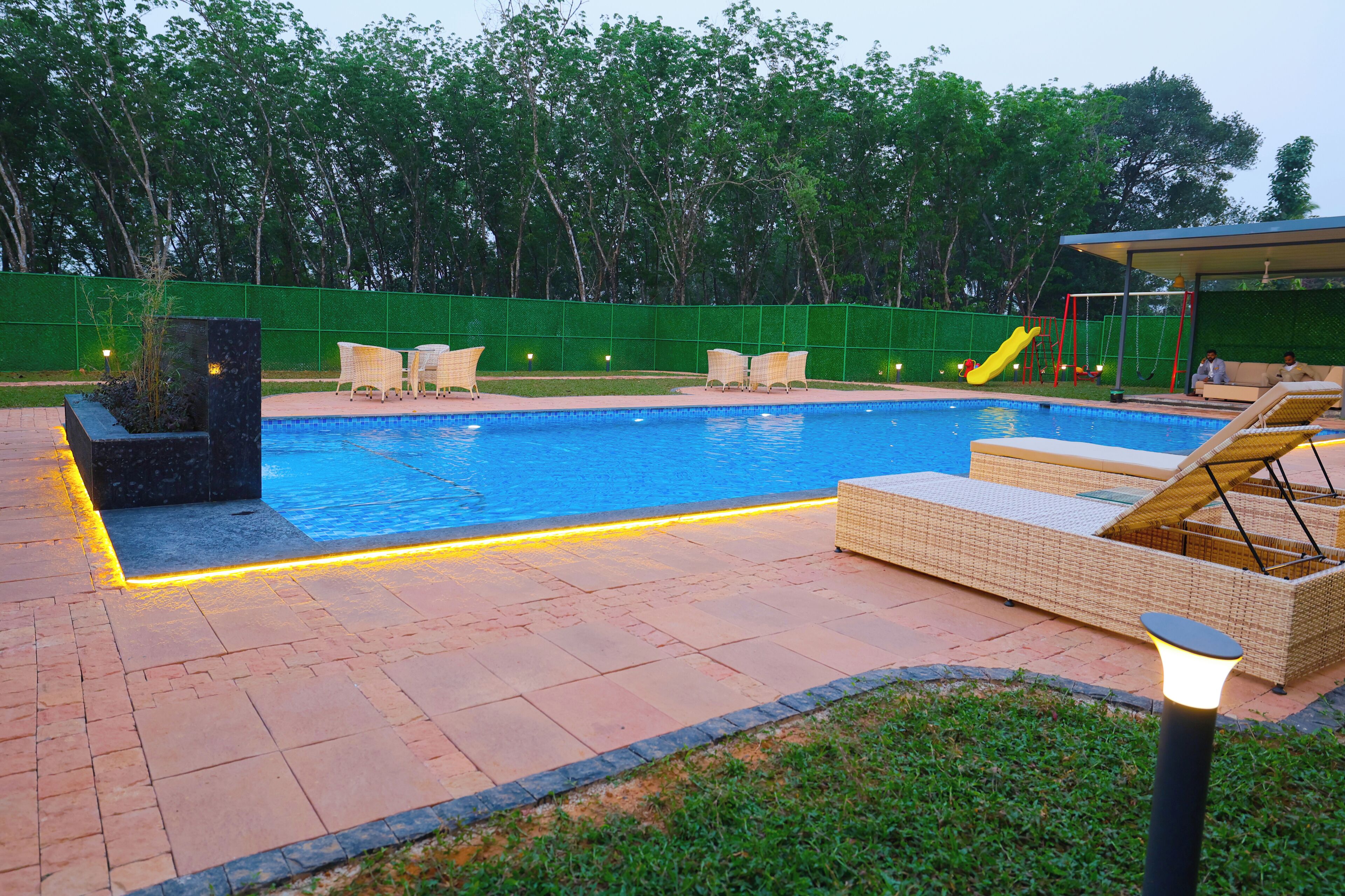 Una piscina con sillas de descanso, un tobogán y una valla verde.