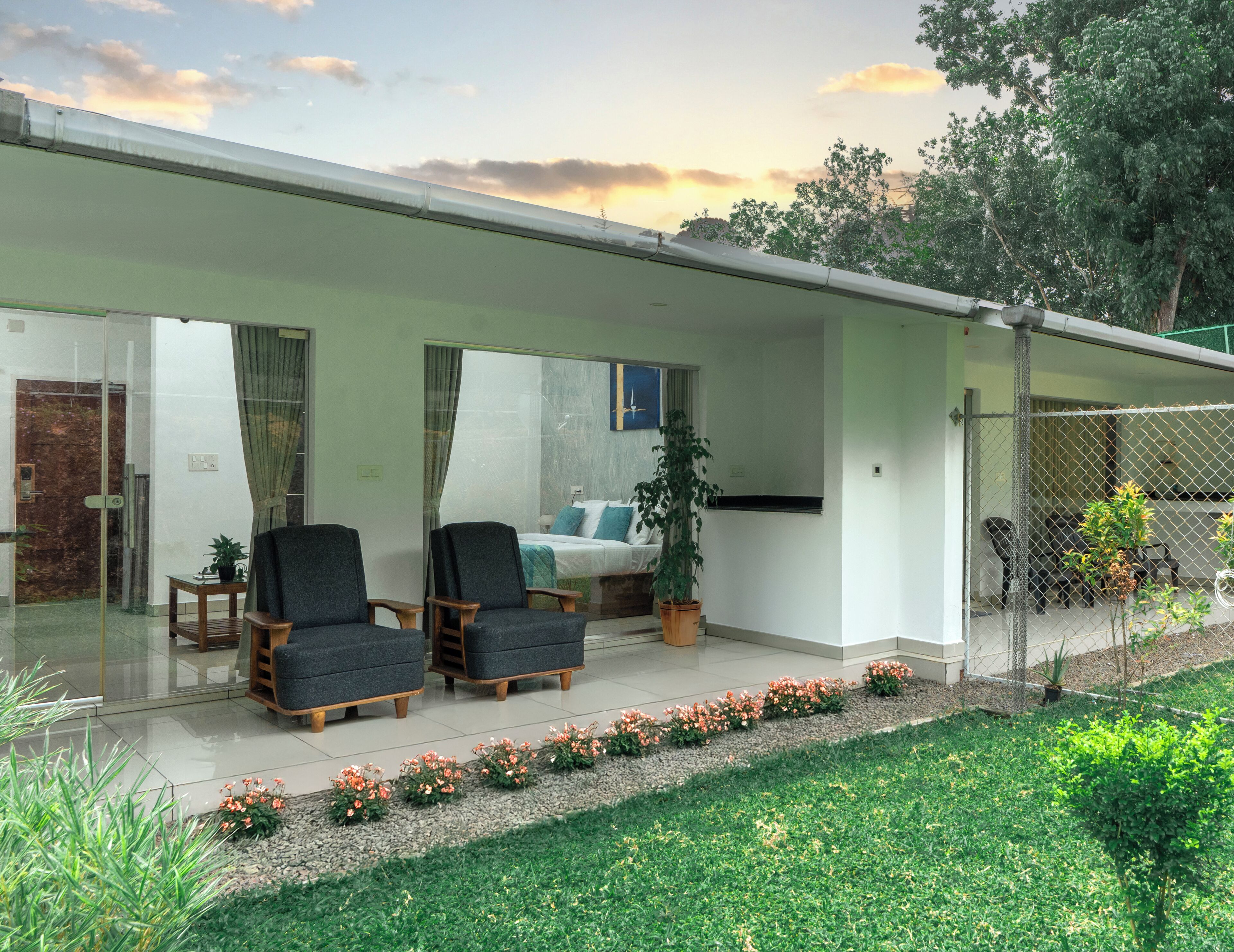 A modern house with a covered patio, two chairs, a potted plant, and a view of the sky.