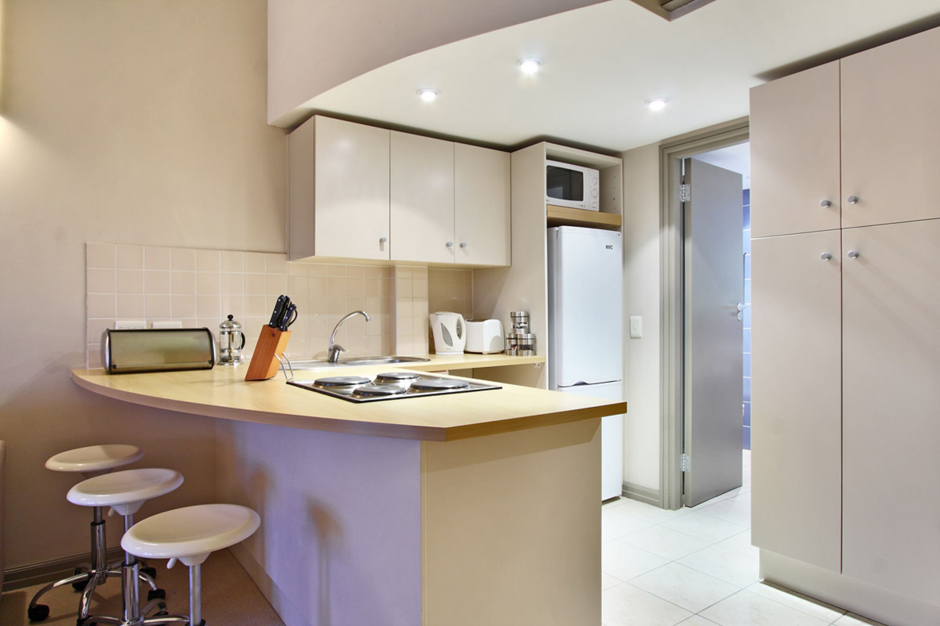 A modern kitchen with a curved island, bar stools, a microwave, and a refrigerator.