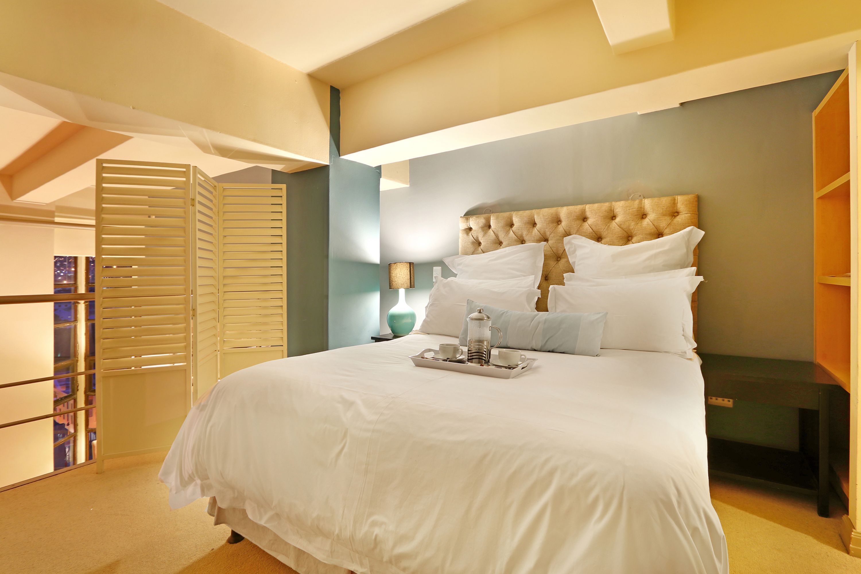 A neatly made bed with a tray of breakfast items, a tufted headboard, and a view of a cityscape through a window.