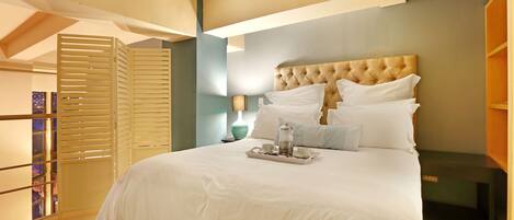 A neatly made bed with a tray of breakfast items, a tufted headboard, and a view of a cityscape through a window.
