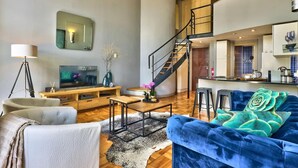 A modern living room with a sofa, coffee table, and TV. A staircase leads to an upper level. - Cape Eazi Stayz Mutual Heights (Cape Town)