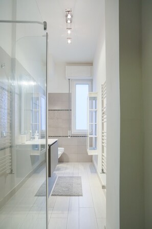 Een moderne badkamer met een douchecabine van glas, een toilet, een wastafel en een raam voor natuurlijk licht.