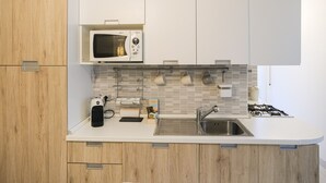 Uma cozinha moderna com armários brancos, micro-ondas, pia e fogão a gás.