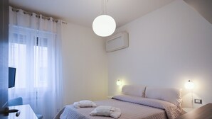 Quarto de hotel minimalista com cama, abajures, escrivaninha e televisão.