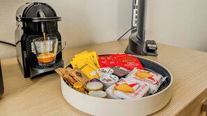 A coffee maker with a cup of coffee, a bowl of assorted tea bags, and a computer monitor on a desk. - Modern Studio Lingotto Historic District (Torino)