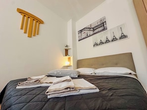 Ein ordentlich bezogenes Bett mit gefalteten Handtüchern, einer Nachttischlampe und Wandbildern mit dem Eiffelturm.