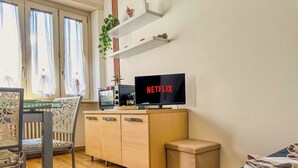 A modern bedroom with a bed, a TV displaying 'NETFLIX', a wooden cabinet, a chair, and a window with curtains. - Modern Studio Lingotto Historic District (Torino)