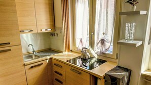 A compact kitchen with wooden cabinets, a sink, and a window with curtains. - Modern Studio Lingotto Historic District (Torino)