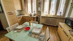 A compact kitchen with wooden cabinets, a dining table set with plates and glasses, and a microwave on the counter. - Modern Studio Lingotto Historic District (Torino)