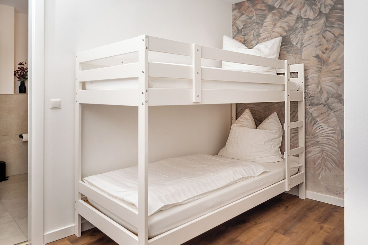 A bunk bed with a ladder, white bedding, and a wooden floor.