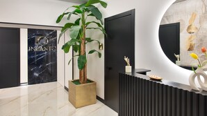 Et moderne receptionområde med en marmorgulv, en stor stueplante, en sort receptionsdisk og et rundt spejl monteret på væggen.