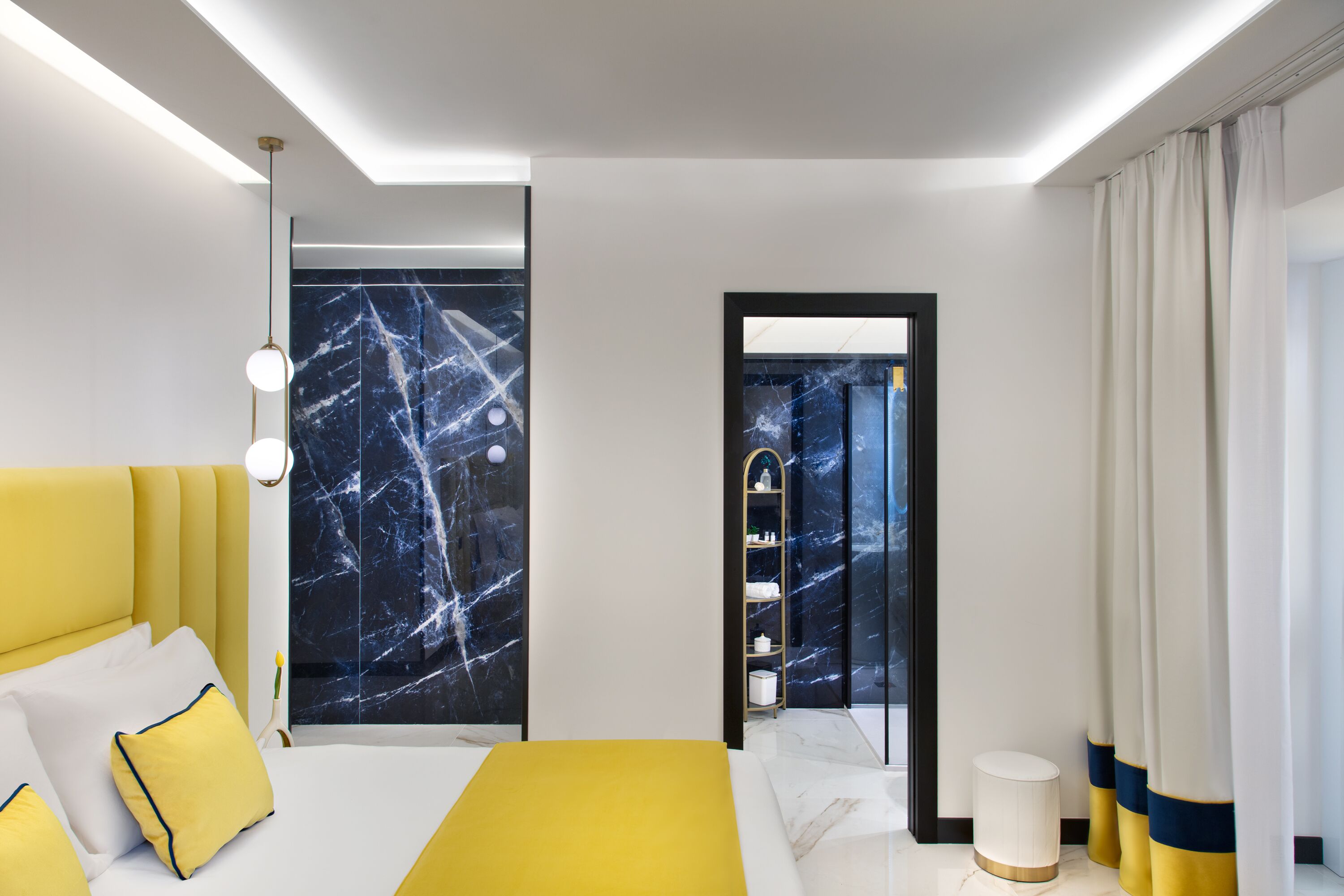 Une chambre d’hôtel moderne avec un lit jaune, un mur en marbre et une vue sur la ville, visible à travers une porte vitrée.