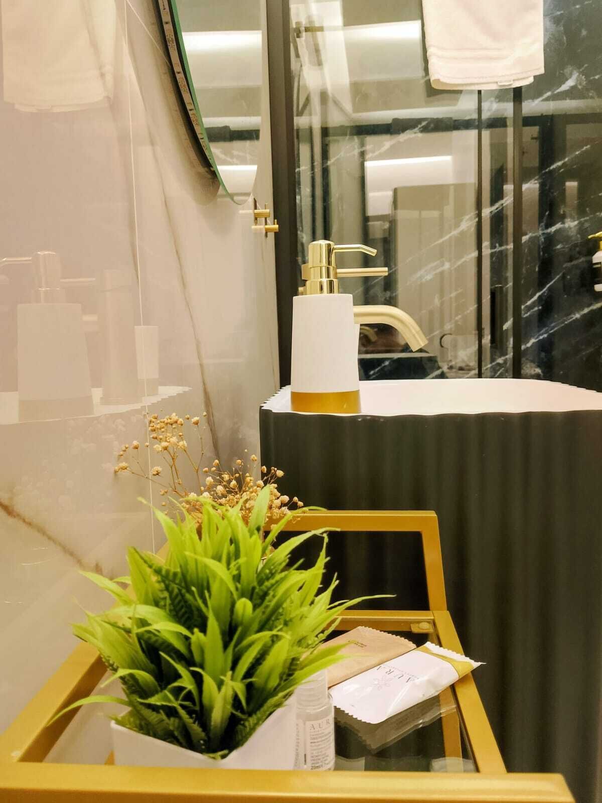 A bathroom with a white sink, gold faucet, and a mirror. There is a plant on a tray and a bottle of lotion on the counter.