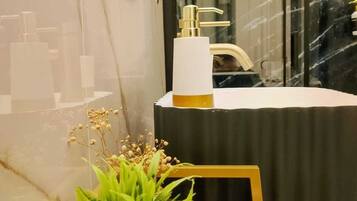 A bathroom with a white sink, gold faucet, and a mirror. There is a plant on a tray and a bottle of lotion on the counter.