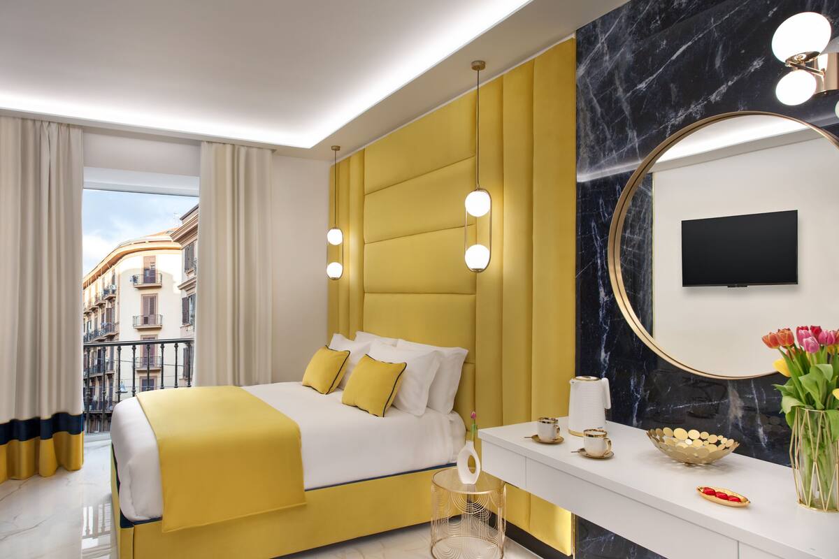 A modern hotel room with a yellow bed, a large mirror, and a view of the city.