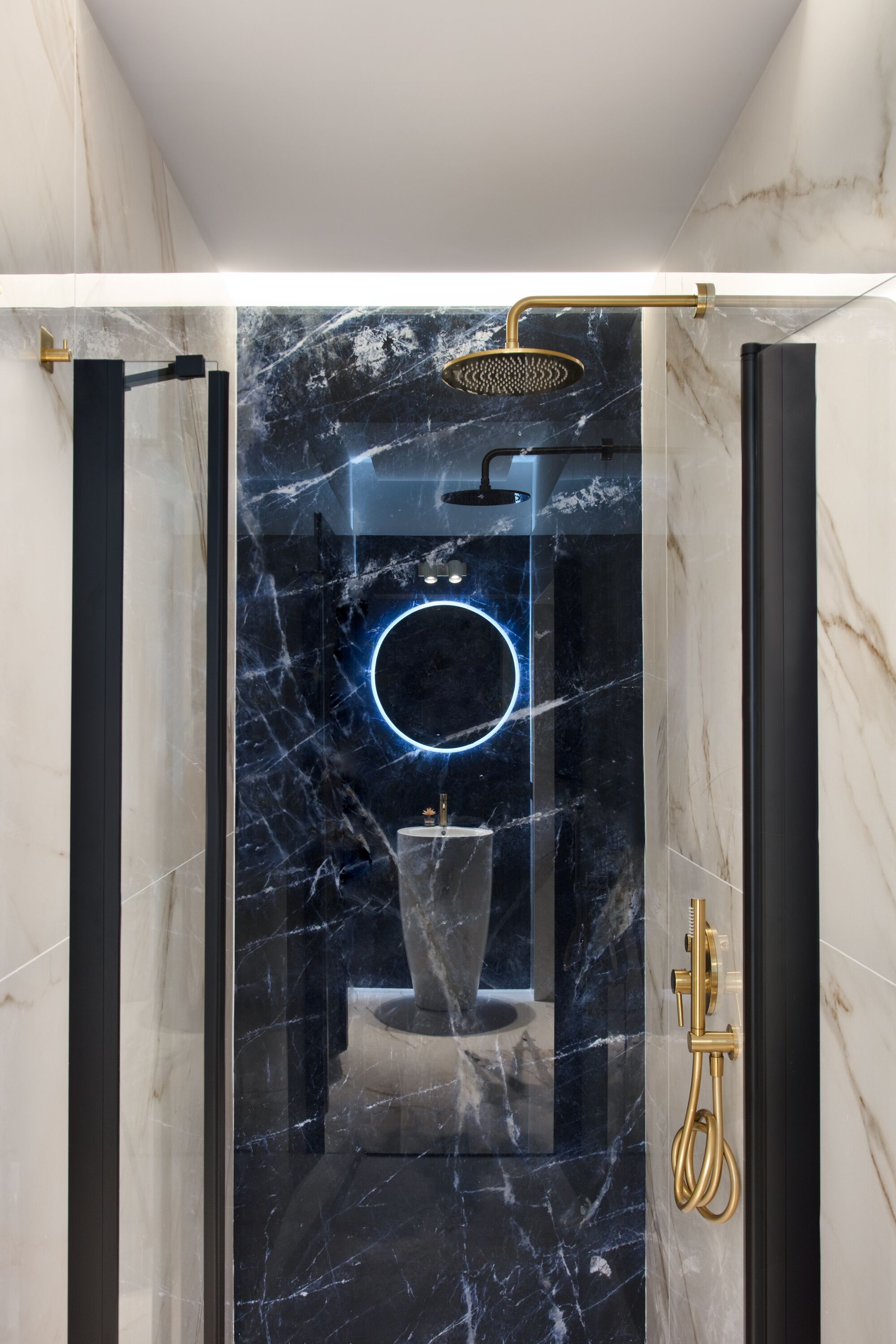 A modern bathroom with a glass-enclosed shower, marble walls, and a circular neon light.