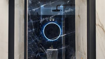A modern bathroom with a glass-enclosed shower, marble walls, and a circular neon light.