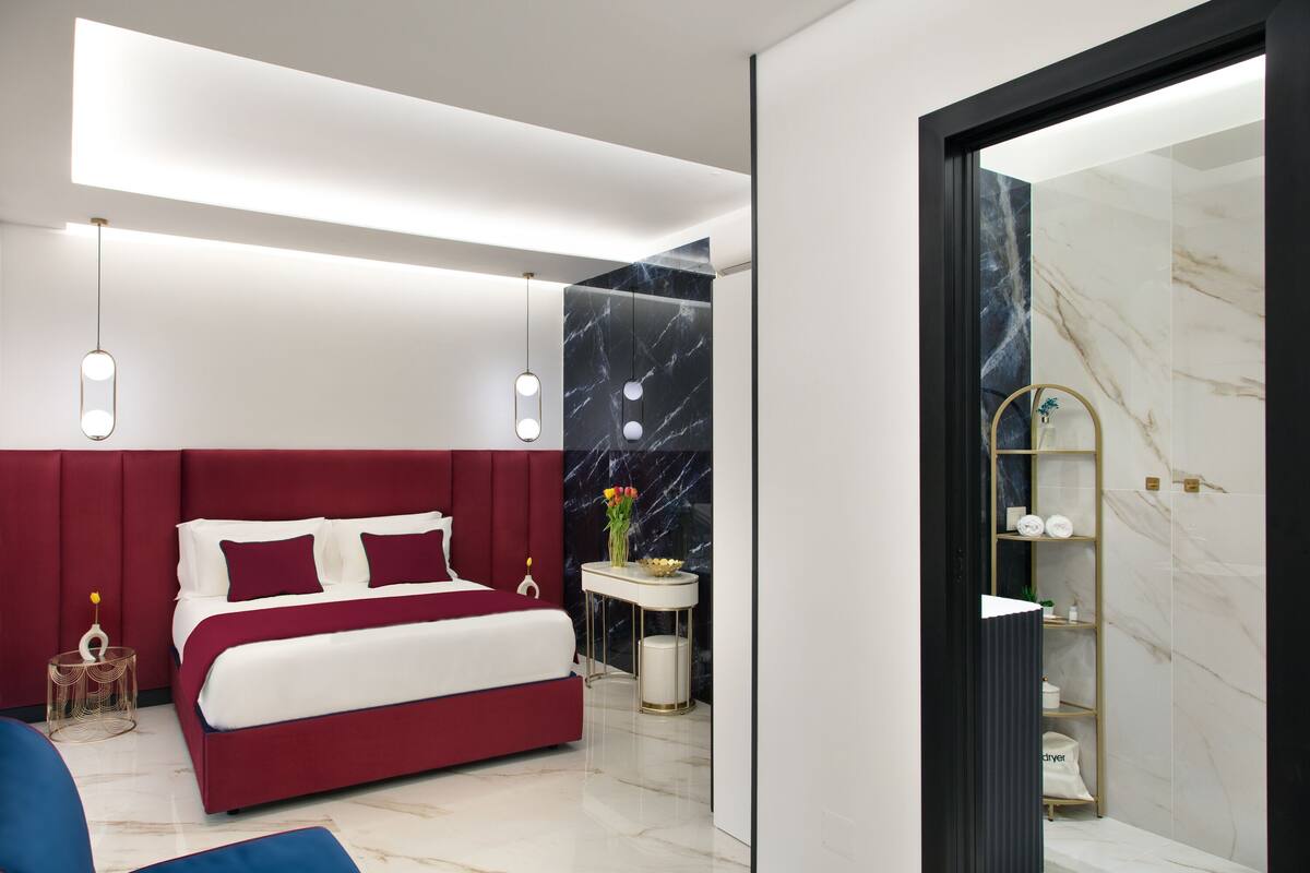 A modern bedroom with a red bed, white bedding, a marble accent wall, and a small bedside table with a vase of flowers.