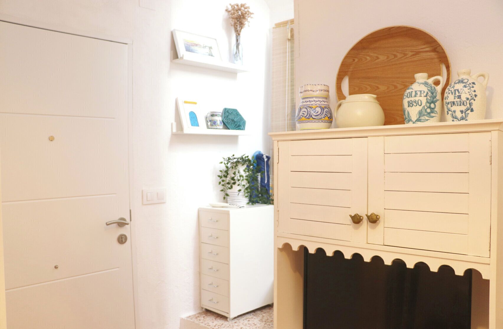 A room with a white door, a white dresser with drawers, a small plant, and decorative items on top.