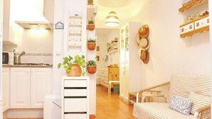 A cozy living room with a striped sofa, a small table, and a kitchen area with white cabinets and a microwave.