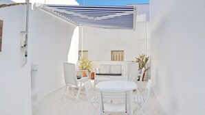 A white outdoor patio with a round table and chairs, a sofa, and a striped awning.