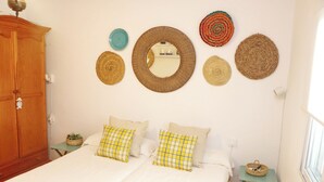 A bedroom with two beds, a wooden wardrobe, and a wall adorned with woven baskets.