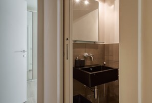 A modern bathroom with a black sink, a glass shelf above it, and a mirror.