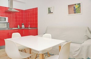 Une cuisine de taille réduite avec des carreaux rouges, une table à manger blanche et un canapé gris.