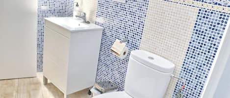 A bathroom with a white toilet, a white sink with a mirror, and a tiled wall with a blue and white pattern.