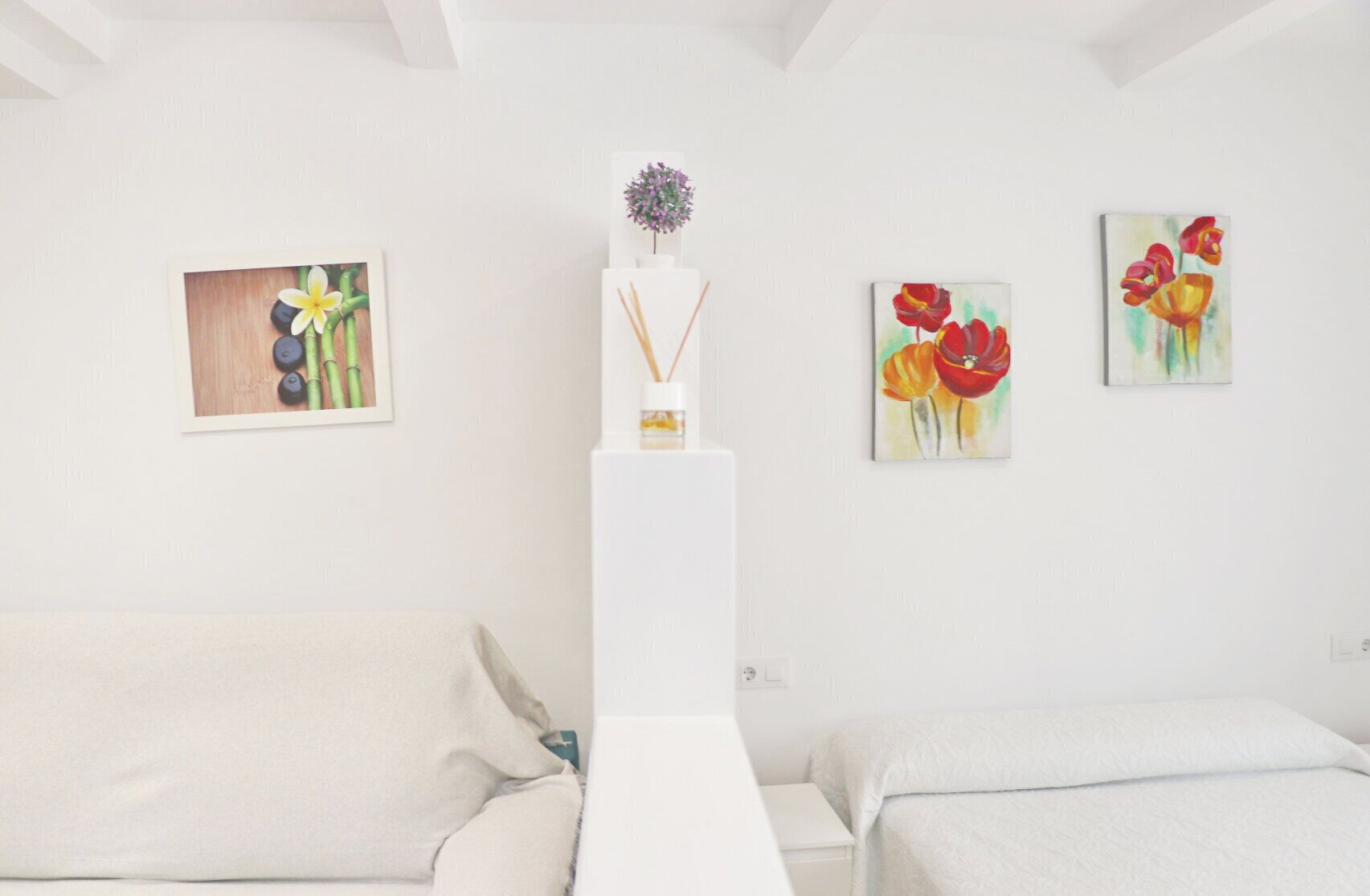 A minimalist room with a white bed, a white nightstand, and three paintings on the wall.