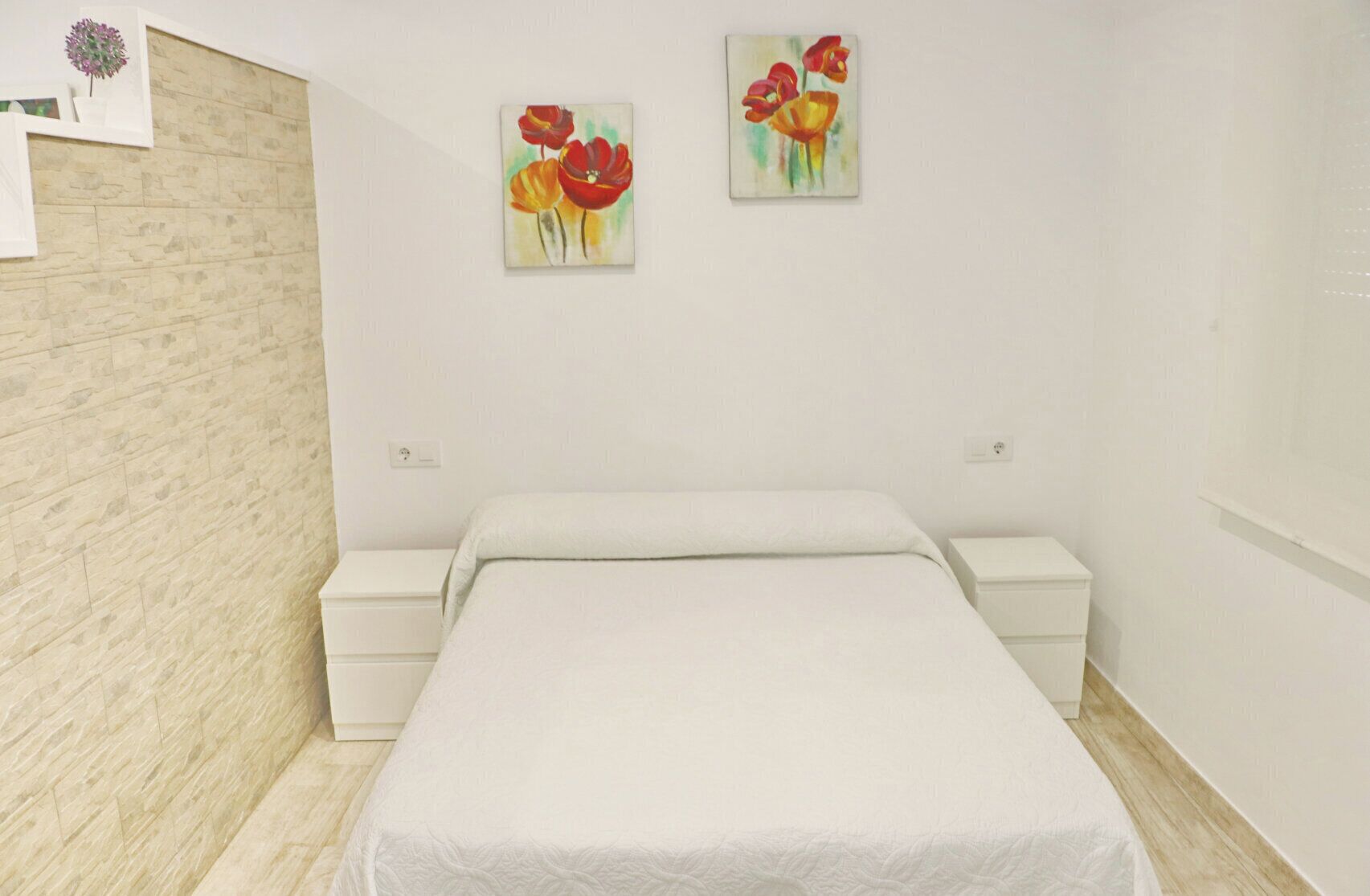 Un dormitorio con una cama, dos mesitas de noche y dos cuadros en la pared.