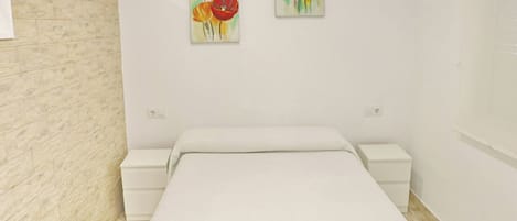 Un dormitorio con una cama, dos mesitas de noche y dos cuadros en la pared.