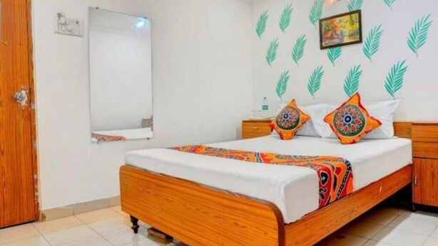 A bedroom with a wooden bed, a white wall, a mirror, and a patterned pillow. - Hotel  Super  (Mumbai)