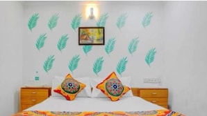 A bedroom with a bed, two nightstands, a wall-mounted light, and decorative leaf decals. - Hotel  Super  (Mumbai)