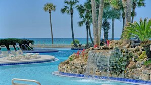 A pool area with lounge chairs, a waterfall feature, and palm trees.